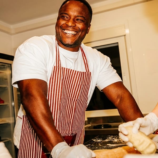 Smiling chef in a red and white striped apron preparing food with two other people.